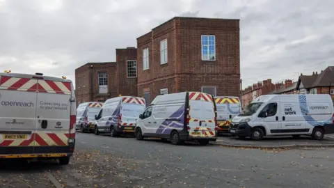 BBC Multiple white vans with broadband company branding parked outside a brick building near Trent Bridge, Nottingham