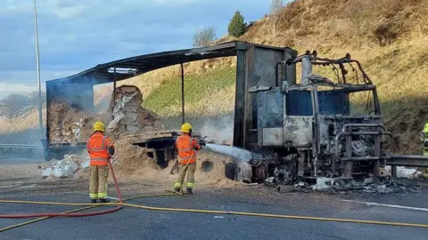 West Yorkshire Fire and Rescue Service A burnt out lorry at the side of a carriageway on the M62