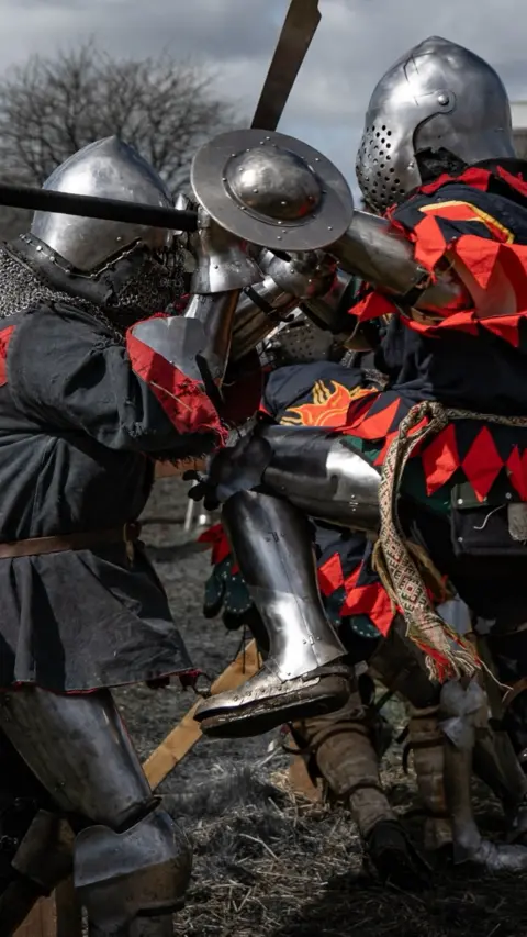 People in medieval armour fighting with swords.  