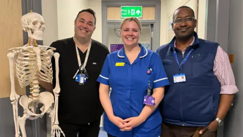 Somerset NHS Foundation Trust A life-size skeleton ornament, with three clinical employees stood in a line. They are smiling into the camera.