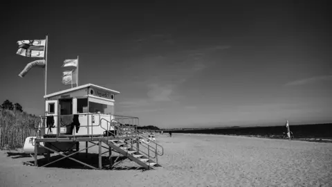 Andrew Henderson Black and white view of a beach safety hut on a beach.