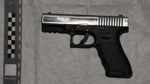 ERSOU A black pistol with a silver barrel. It has been laid out on a white sheet.