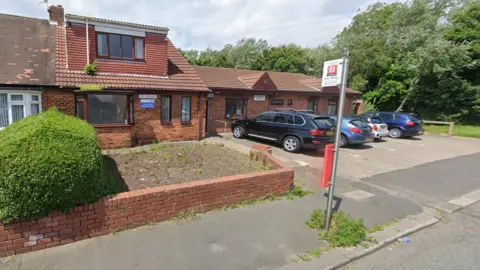 Castletown Medical Centre is a two-storey red brick building. There is blue and white sign at the front of the building with the NHS logo on it. 