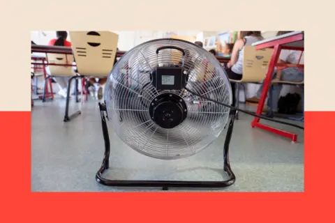Getty Images Close-up of a fan cooling pupils in a classroom in Poitiers, France. Chairs, tables and the backs of pupils are also visible. There is a red and beige backdrop.