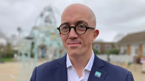 A bald man wear round dark green glasses, white shirt,
