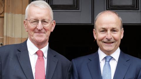 Hilary Benn in a red tie and white shirt with blue blazer met with Micheál Martin in blue blazer and white shirt blue tie, stood in front of doors of hillsborough castle 