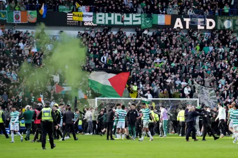 PA Media Green smoke over a stand full of Celtic fans at Ibrox - a few of the fans are waving Palestinian flags