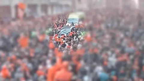 Blurred footage with exposed section showing Doyle driving through a crowd
