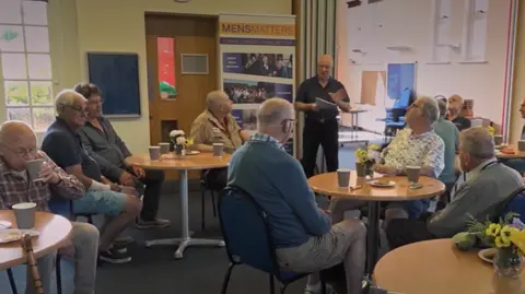 Men's Matter A group of men aged between 60 and 70, are sitting at several tables drinking tea, eating biscuits and taking part in a quiz.