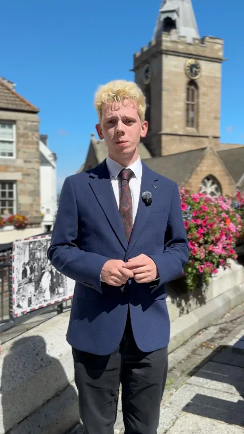 A man with blonde hair wearing a blue suit looking at the camera