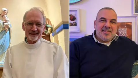 Two men smiling, the one on the left is wearing a white vicar's outfit with adog collar. The man on the right is sitting in front of art and wearing a blue jumper and stripy shirt