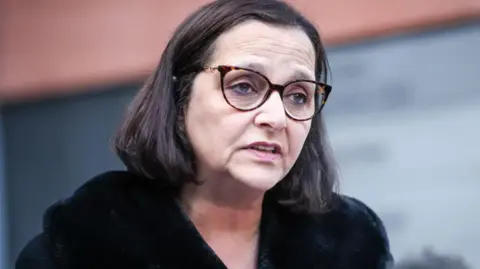 PA Media Figen Murray, the mother of Martyn Hett, with bobbed dark brown hair wearing tortoise shelled glasses and a black coat with a black faux fur lapel.