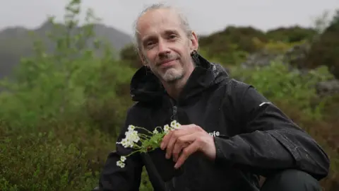 BBC/Guyndaf Hughes Robbie Blackhall-Miles holding a pink saxifrage
