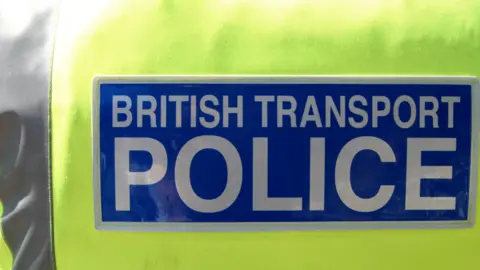 A generic photo of a yellow hi-vis. The words British Transport Police are in white letters on a blue background. 