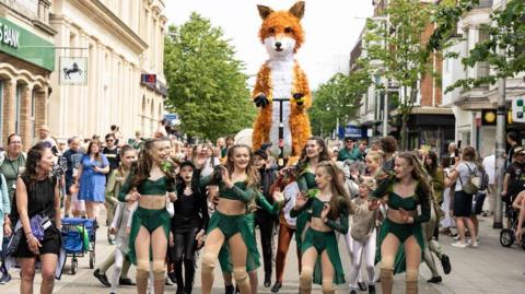 Dancers and shoppers encircle a giant fox puppet called Farrah in Lowestoft  