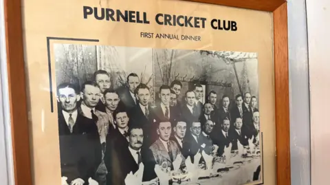 Purnell Cricket Club A framed black and white photo of Purnell Cricket Club's first annual dinner, showing about 30 men in suits standing in rows behind a set table.