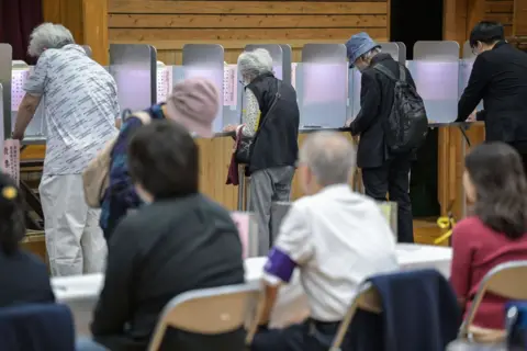 Getty Images Para pejabat mengamati orang-orang yang memberikan suaranya selama pemilihan umum di tempat pemungutan suara yang didirikan di sebuah sekolah lokal di Tokyo pada 27 Oktober 2024.