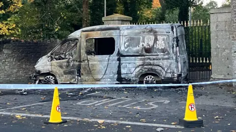 BBC A burnt out police vehicle behind a cordon