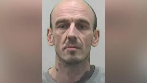 Northumbria Police Mugshot of Richard Temple. He has tattoos on his neck and a craggy face with a cut on his lip. He has short stubble and a shaved head.