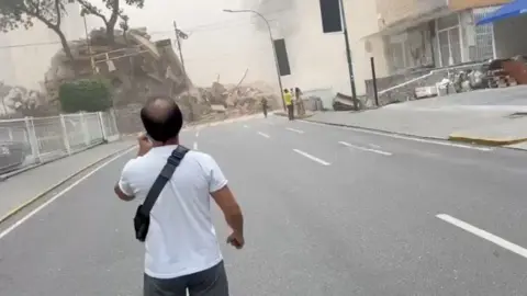 A man stands on a street staring towards a collapsed building.