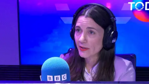 Lauren Schultz on the Today programme set with big headphones on, talking into a BBC microphone.