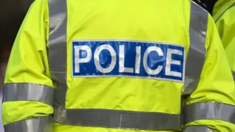 Getty Images The back of a police hi-vis jacket. It has grey strips and a blue rectangle to the centre with the word 'Police' written in white.