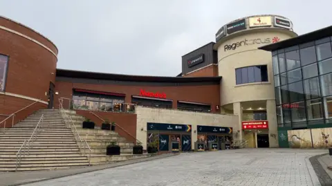 The Regent Circus complex with a Nandos sign prominently displayed on a grey day. The steps up to the second level appear prominently on the left of the picture.