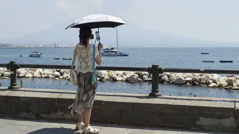 Getty Images A woman uses an umbrella to shield herself from the sun during the African heatwave in Naples on August 4, 2026.