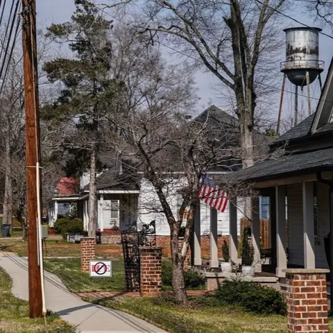 Getty Images A view down a street in Social Circle, with small homes on one side and a white church spire in the distance. On one lawn is a sign that says ICE - crossed out