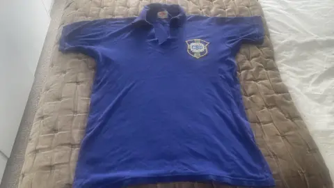 Laurence Bennett A Brazil training shirt has been laid out on a bed. It is a deep blue colour with a collar, and the Brazil crest.