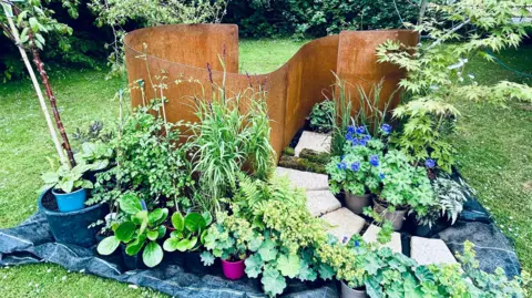 Claudia Sermbezis/BBC The Newborn Garden designed by Jane Eastwood. The design includes a partition, several white bricks and various plants and flowers dotted around the design.