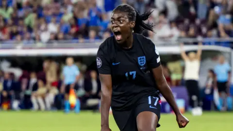 EPA/Shutterstock Michelle Agyemang in a black England top, shouting and running in celebration on a football pitch.