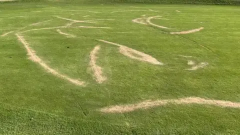 Supplied Shot of damage to a fairway of a golf course. Several long lines of sand have been kicked up, which appear to be made by a motorised bike tyre.