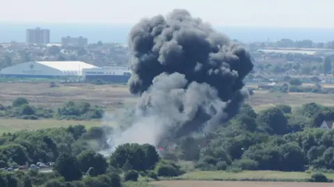 PA Media A huge plume of black smoke rising from a motorway in the aftermath of a plane crashing in Shoreham.