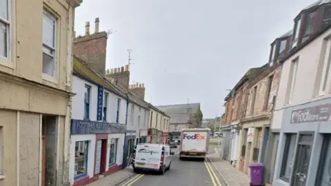 A narrow street with shops on either side and two vans