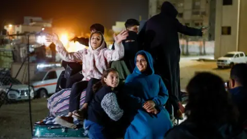 Reuters A woman and children, looking happy, sitting in the back of a pick-up truck at night-time after arriving in Gaza from Egypt