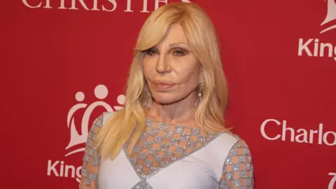 EPA/Shutterstock Donatella Versace poses for picture in front of red King's Trust background