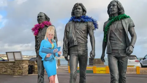 imaginationlibrary.im A cardboard cut out of DOlly Parton infront of the BEE GEE statues 