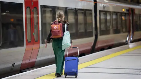 EPA Rail passenger drags her case along a railway platform while carrying a backpack and a bag on her shoulder