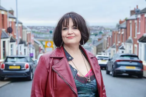 BBC Ruth Jones as Nessa, pictured smiling while wearing a dark red leather jacket on the streets of Barry Island