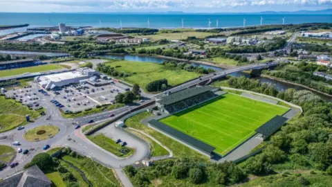 Cumberland Council An aerial CGI of how the Cumberland Sports Village could look. A large pitch is marked out for rugby with a high, single-tiered stand along the far touchline. Smaller covered stands are at one end and on the opposite touchline, while an uncovered stand sits at the other end of the pitch.