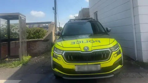 A police car is seen with a blurred out license plate at the scene in Mount Street in Coleraine. A phonebox and shrubbery can be seen beside the vehicle.
