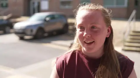 City of Oxford College student Megan has long brown hair and is smiling. She is wearing a sleeveless maroon t-shirt.