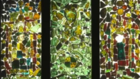 A design of how the window panels will look - a mixture of deep greens with hues of amber and red culminate together into three abstract designs.