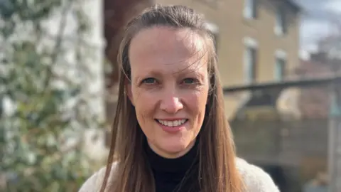 Holly with long brown hair smiling at the camera. She is stood outside in her garden.