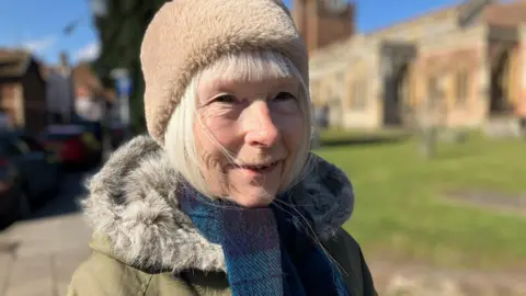 A woman in a furry hat in front of a church on a sunny day