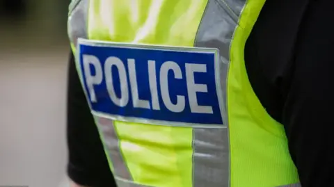 The back view of a British police vest which is bright yellow and has the words police in block white lettering against a blue rectangle background.