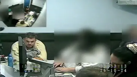 A man with dark hair and a cream jacket sat in a police interview room