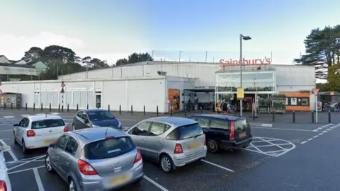 Google Street View image of the Sainsbury's supermarket store in Falmouth. Five cars are parked in spaces in the car park outside the front entrance of the store.
