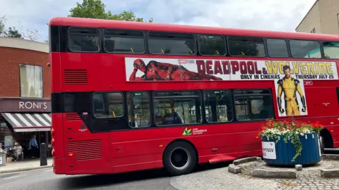 BBC/Harry Low Double decker bus crashed into a roundabout with a large 'Deadpool Wolverine' advert on the side of it